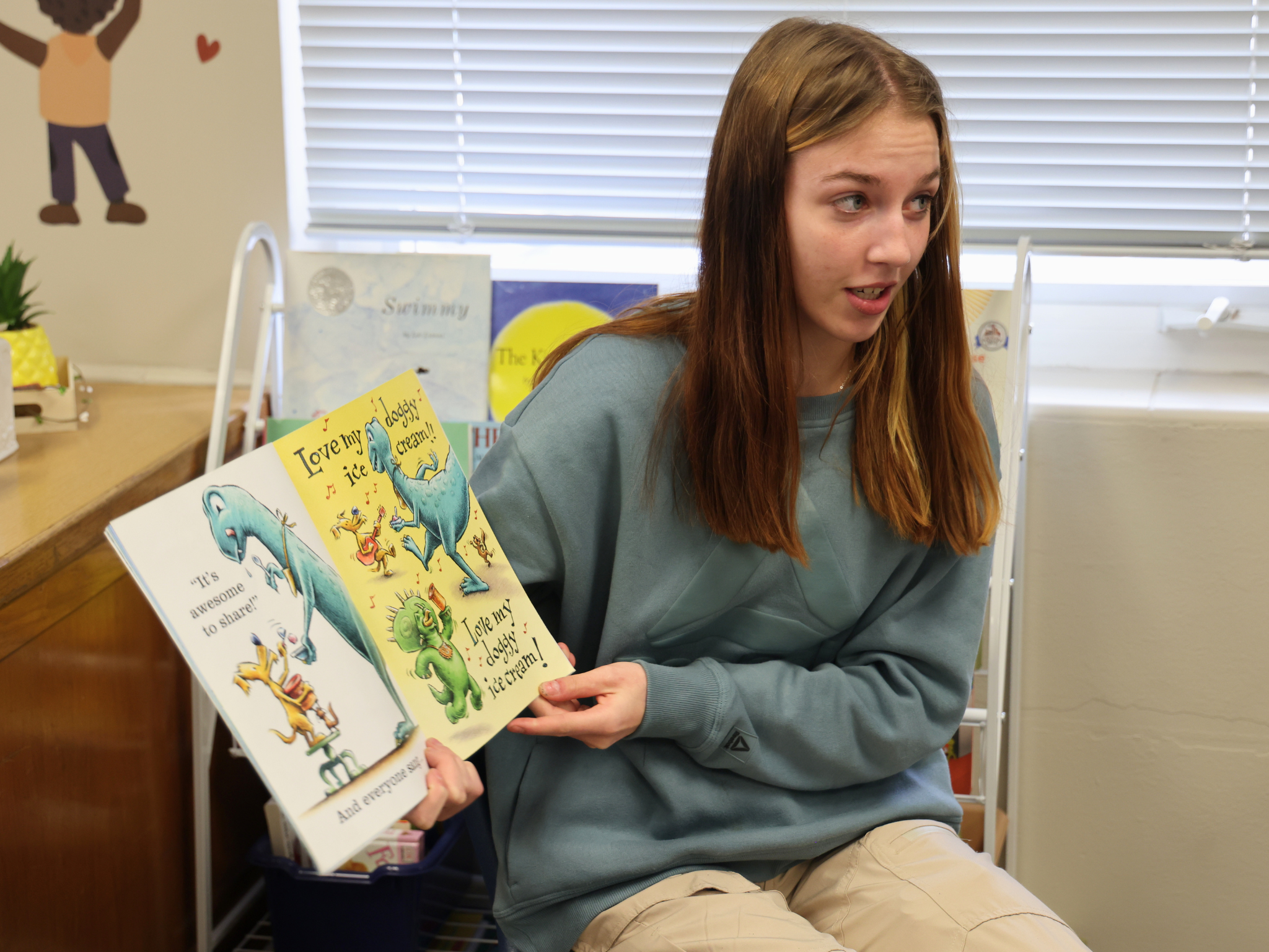 Student reads a picture book to an audience off camera.