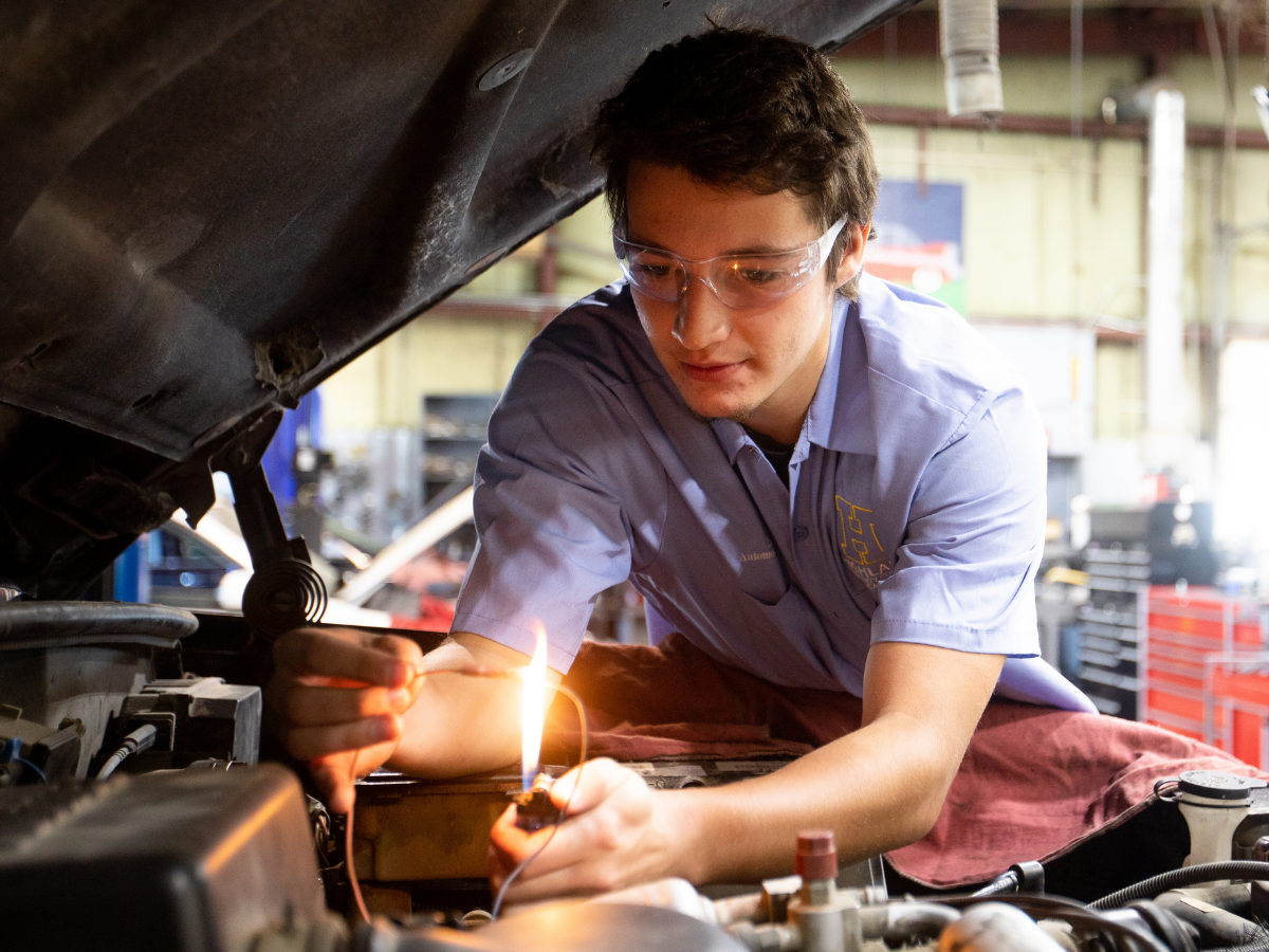 Automotive student leans into the car while working on the engine.