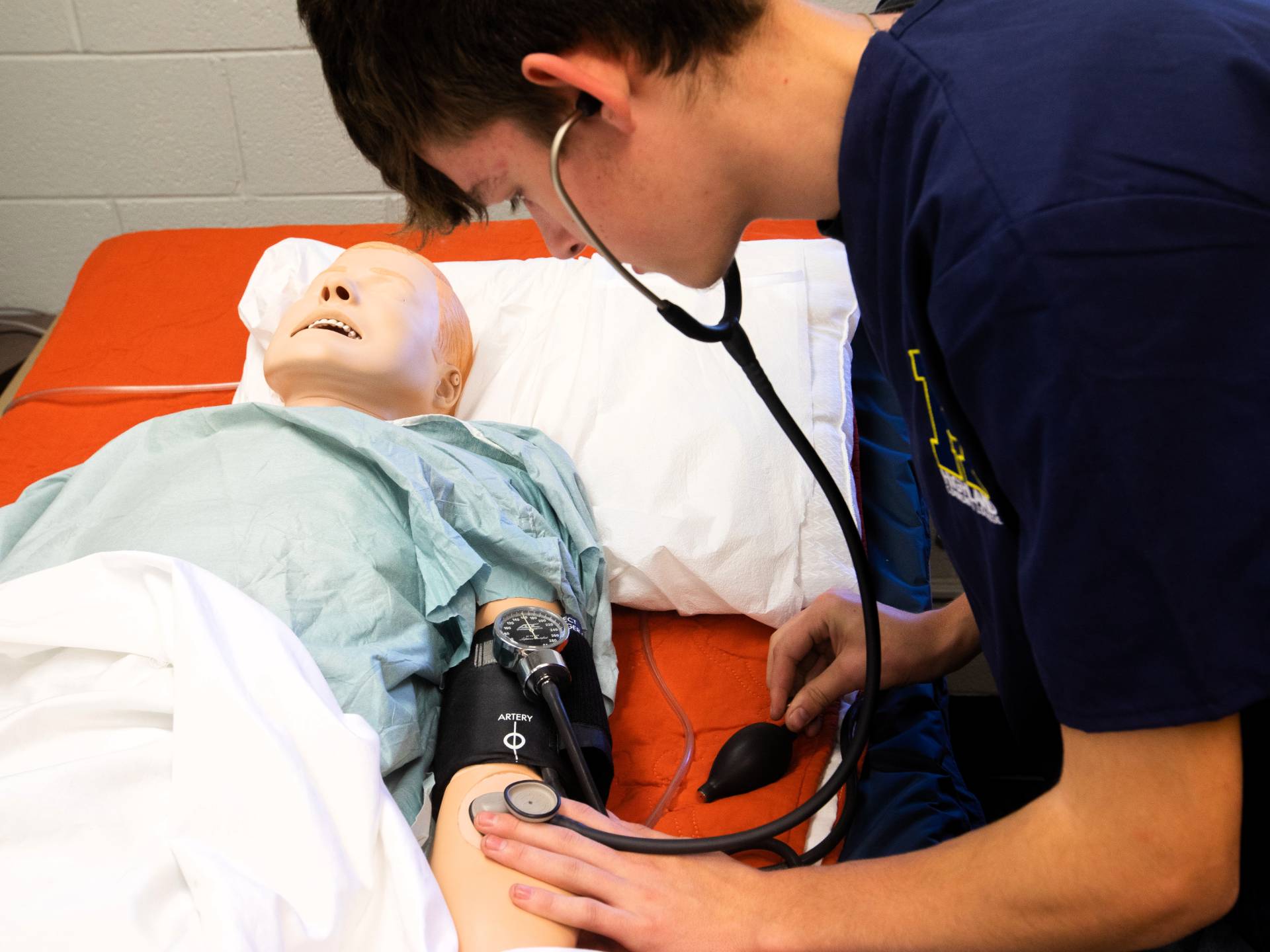 An allied health student practices taking the vitals on a practice doll