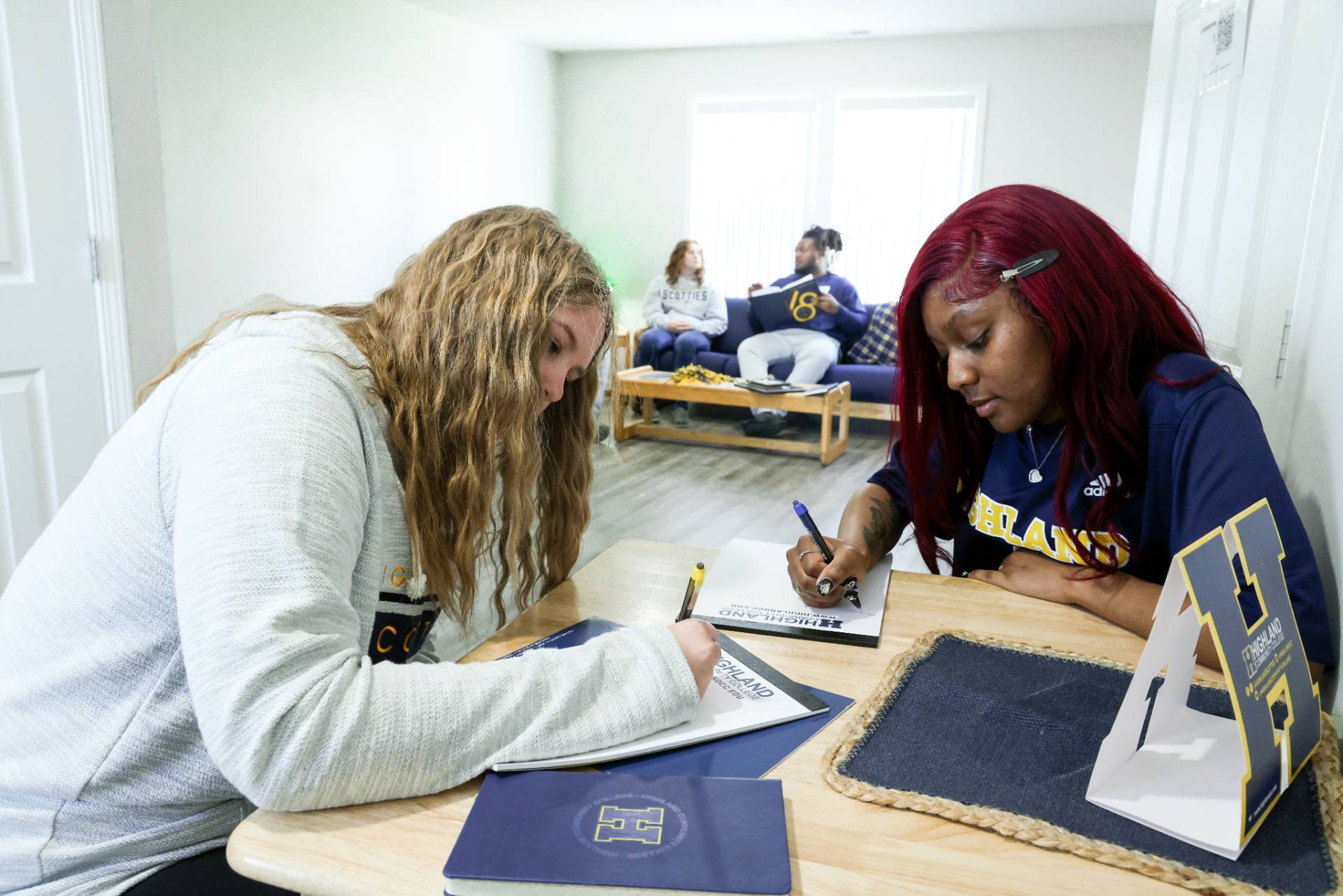 Two students studying at desk with two students sitting toward the back