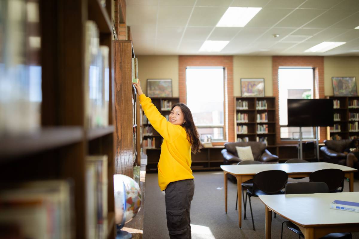 Student in the library reaching for a book on the shelf.