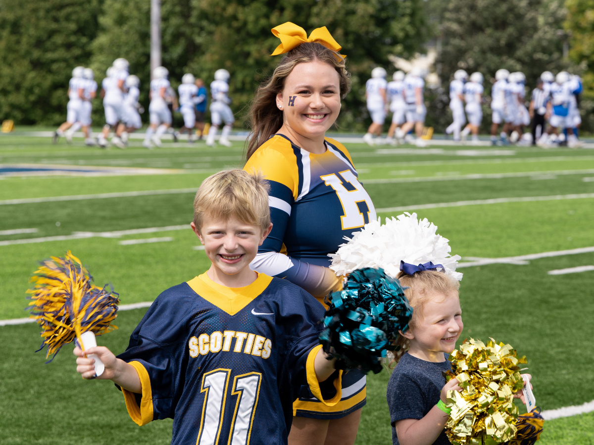 Scottie Cheerleader smiles at the camera while posing with two young scottie fans
