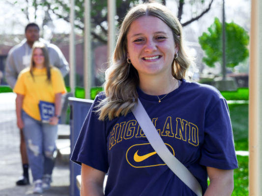 Student in a blue shirt with Highland printed in Gold smiles at the camera. 