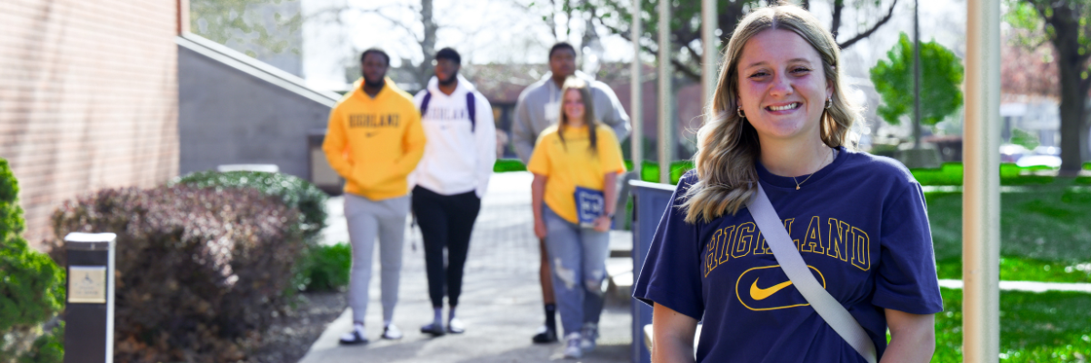Student in a blue shirt with Highland printed in Gold smiles at the camera. 