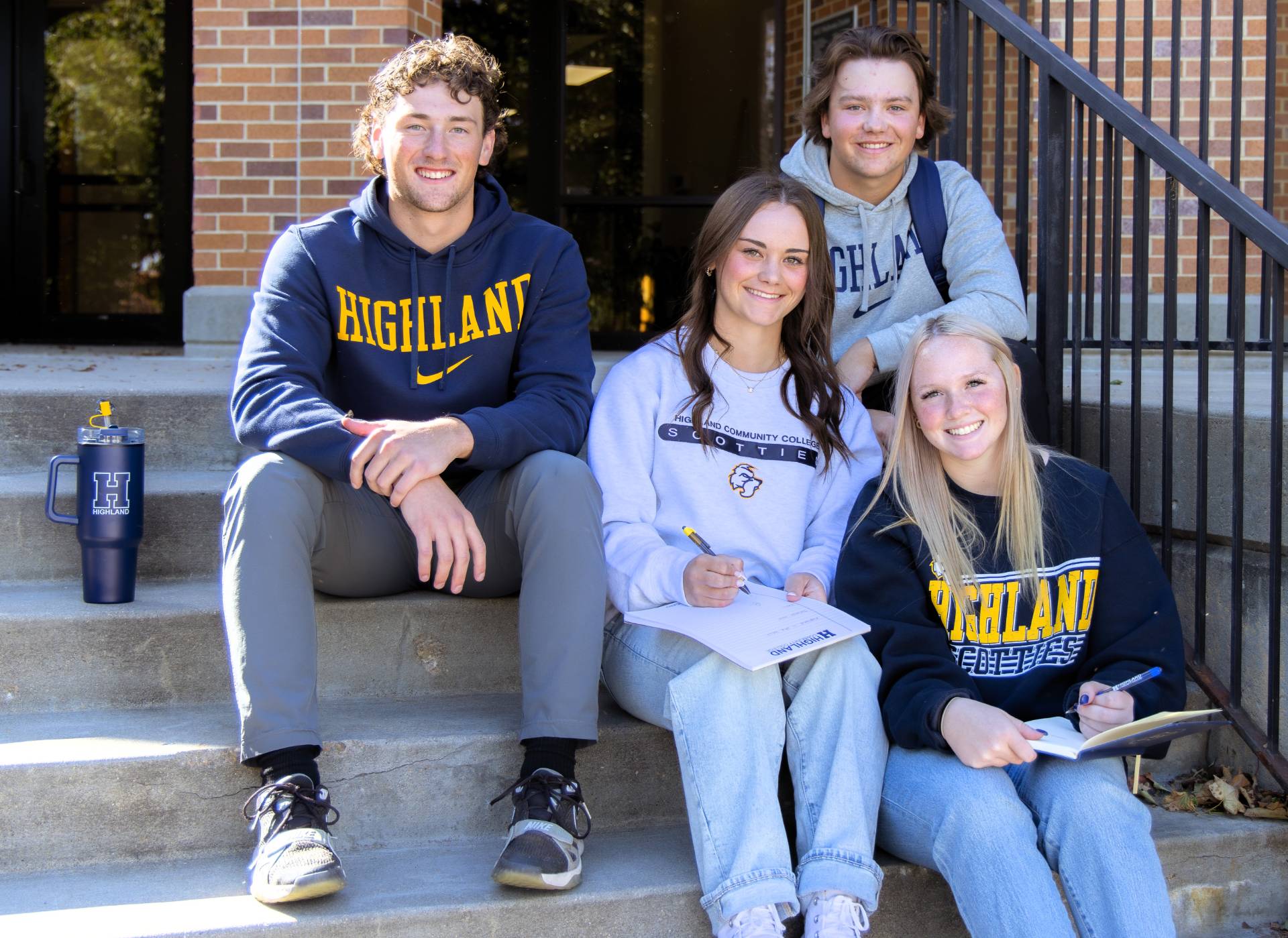 Group of four students sitting on the steps outside the Wellness Center.