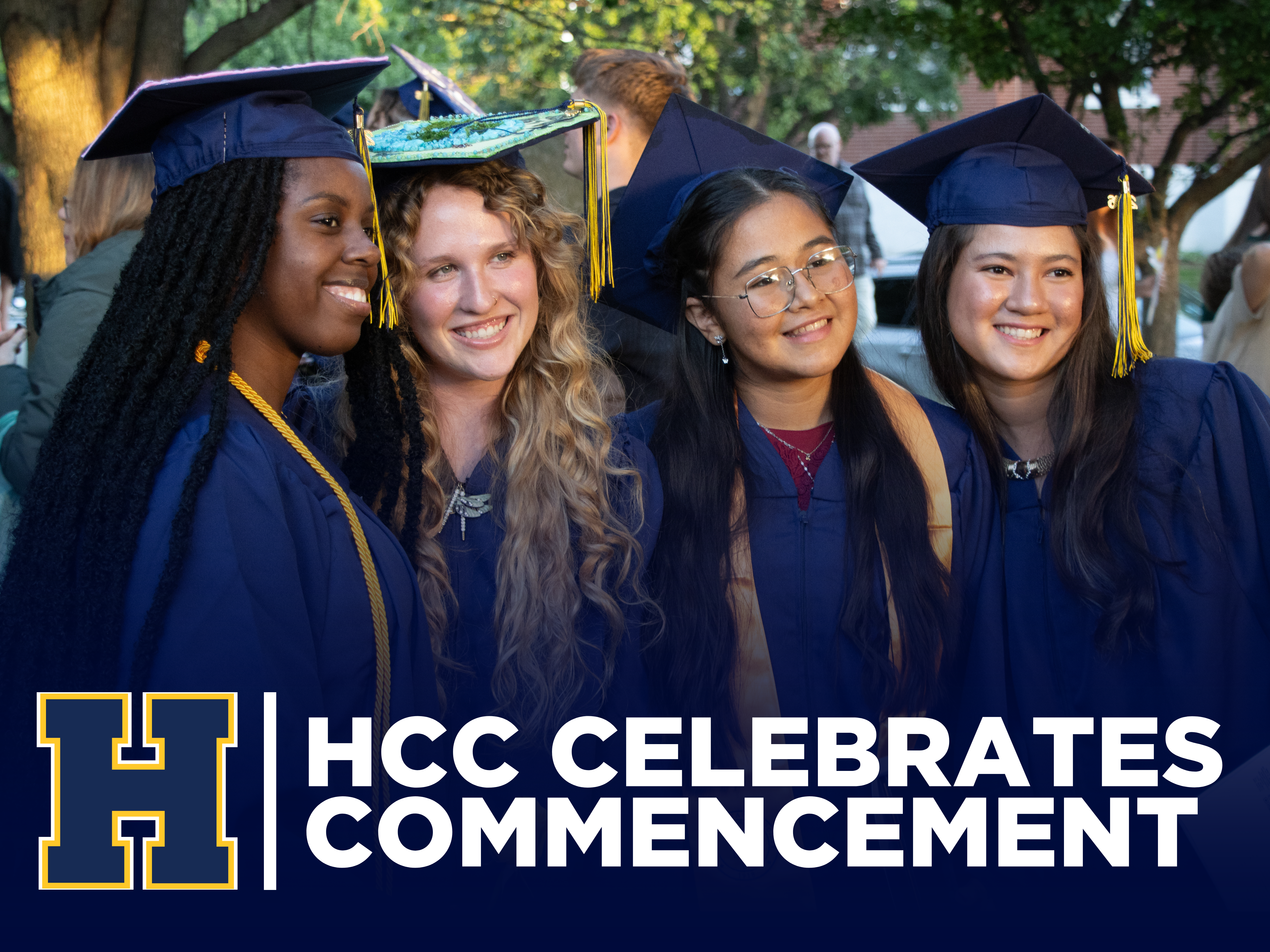 Four graduates pose together at graduation. Flyer says HCC Celebrates Commencement