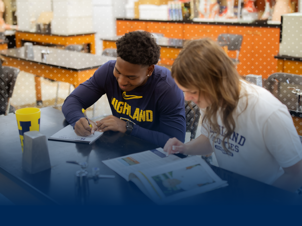 Two students sitting at a table in a science classroom looking at resource materials. 